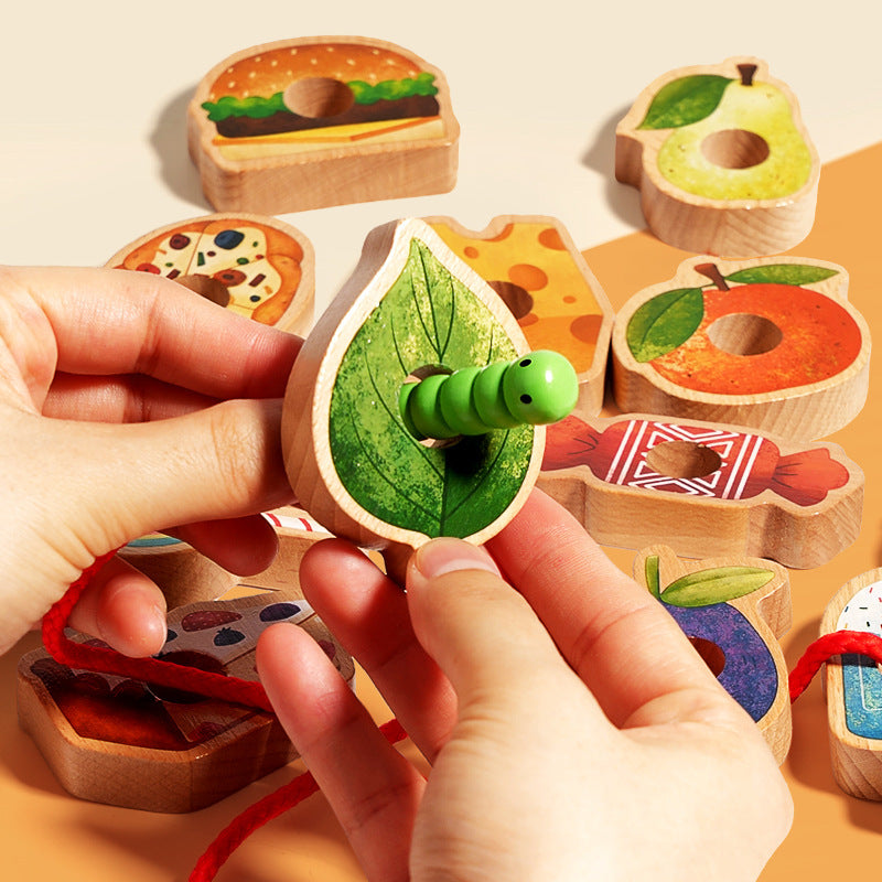 Wooden toy set with colorful pieces and a hand holding a piece with a green caterpillar on a leaf.