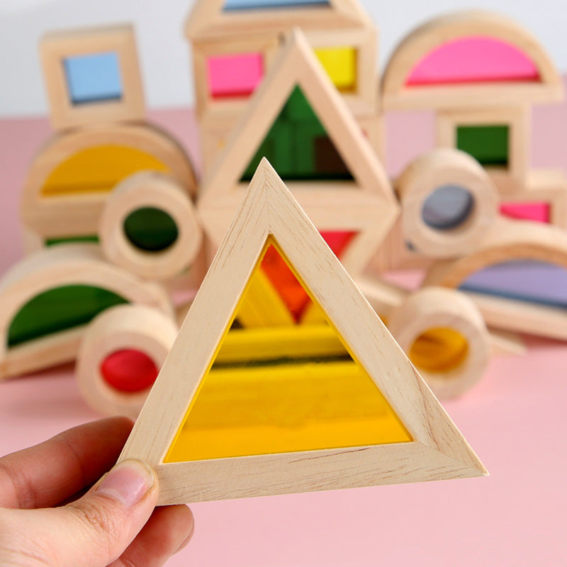 Wooden geometric shape sorter toy with a hand holding a yellow triangle piece against a pink background.