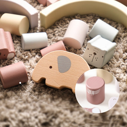 Wooden toys including an elephant and a pink cylindrical block on a carpeted floor.