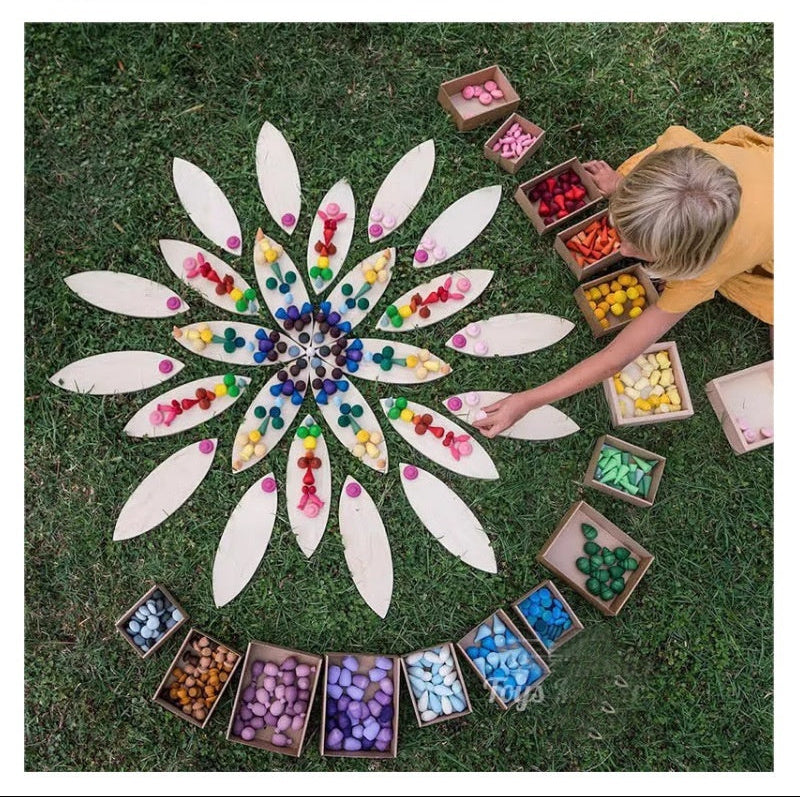 Mandala made with loose parts on grass, surrounded by containers of additional parts.